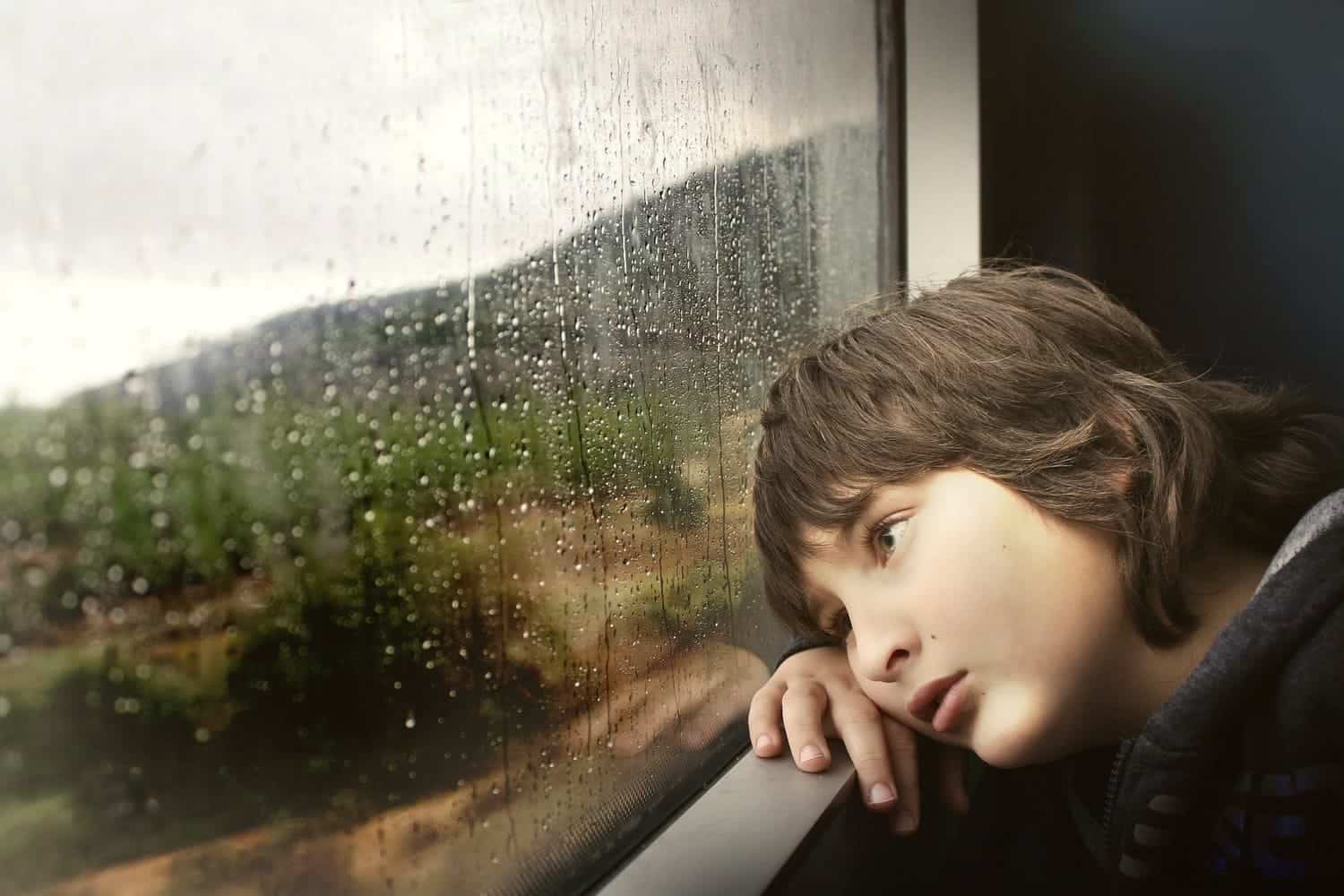 un niño apoyado en una ventana viendo como llueve fuera