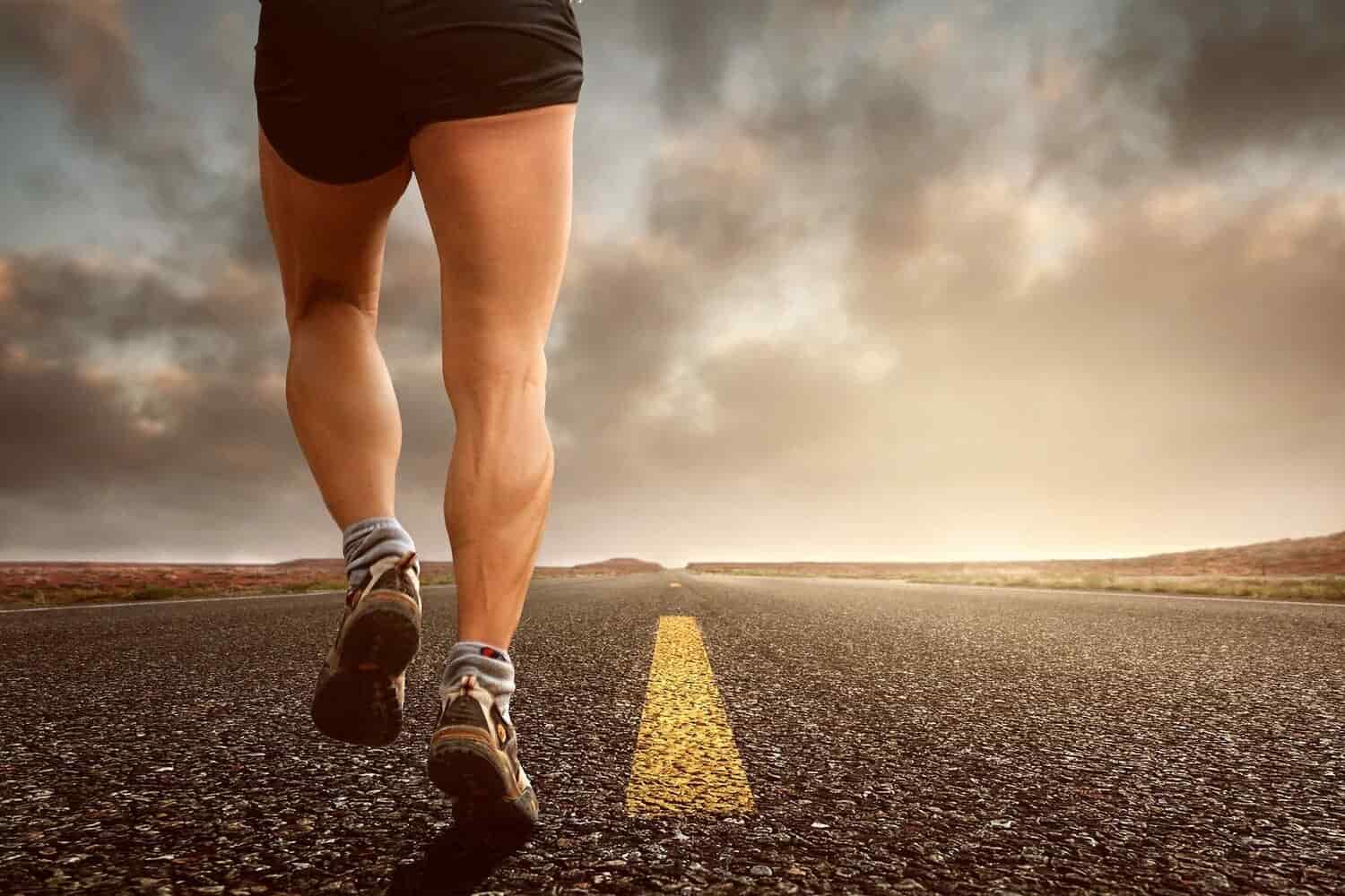 imagen de las piernas de un hombre que va corriendo por una carretera no transitada