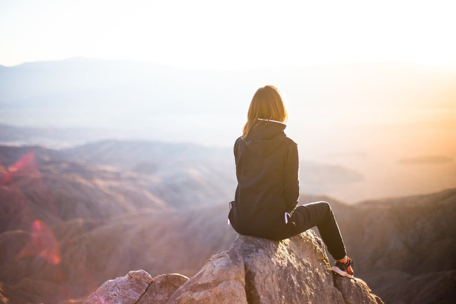 una mujer sentada al borde de una roca que está en la cima de una montaña