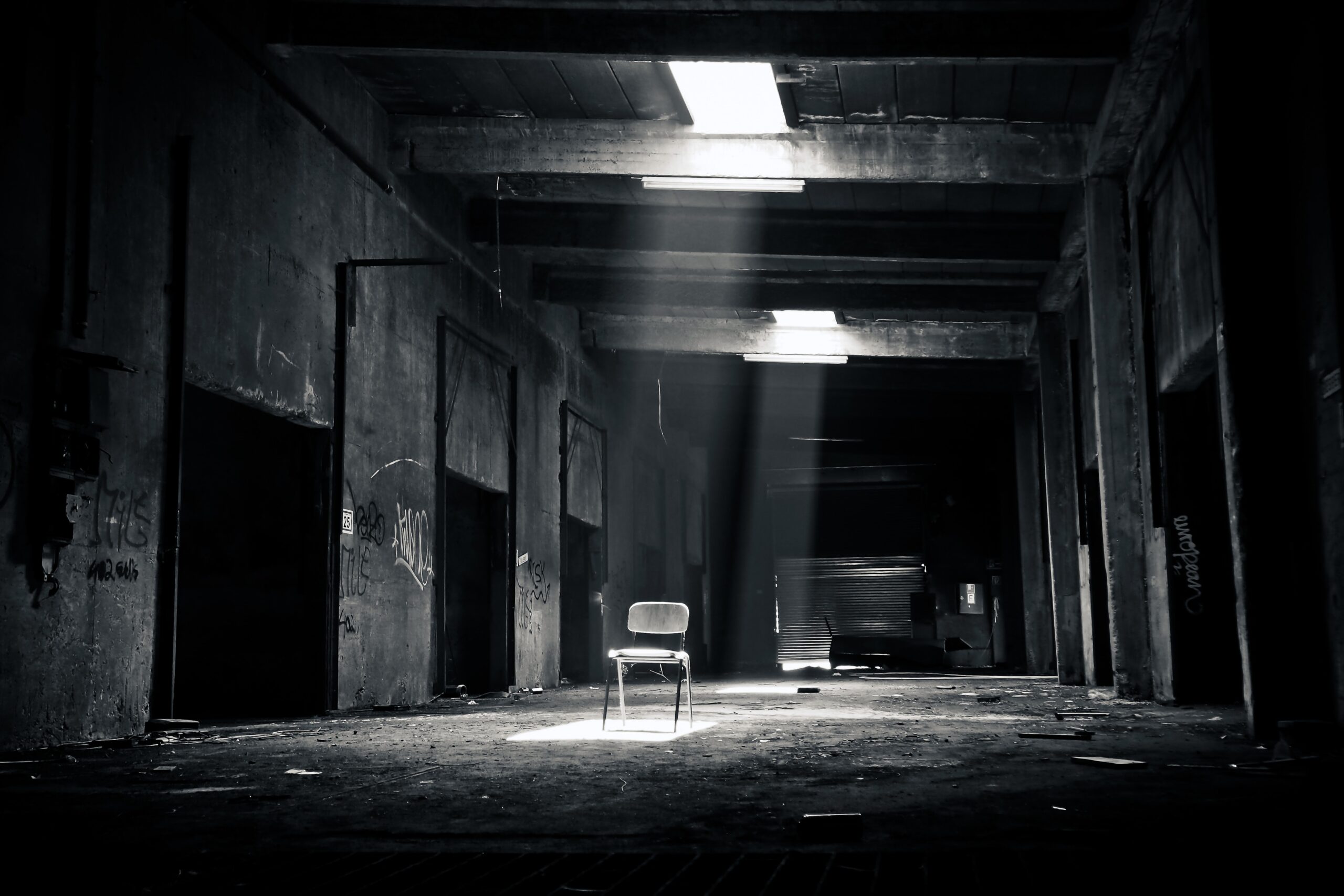 imagen a blanco y negro de un lugar cerrado, abandonado, con poca luz, donde hay una silla en el medio del lugar