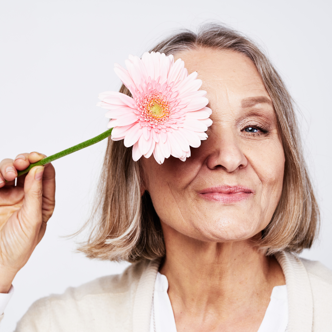 una mujer mayor sonriente con una flor. Imagen que busca hacer referencia a Cómo cómo adaptarse a cambios cognitivos con la edad