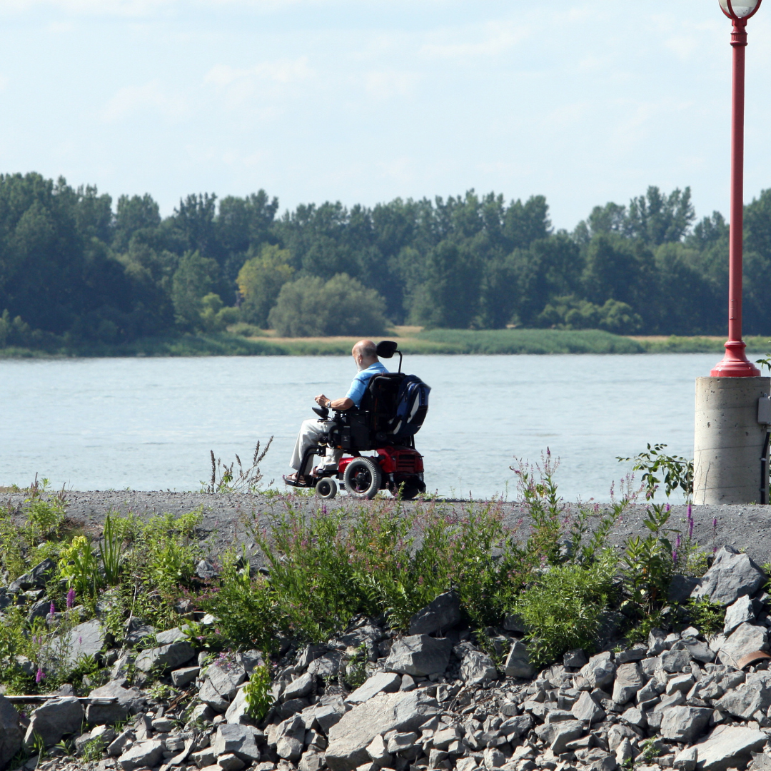 una persona en una silla de ruedas eléctrica dando un paseo a la orilla de un cuerpo de agua. Imagen que hace referencia a la autonomía e independencia de un paciente con daño cerebral