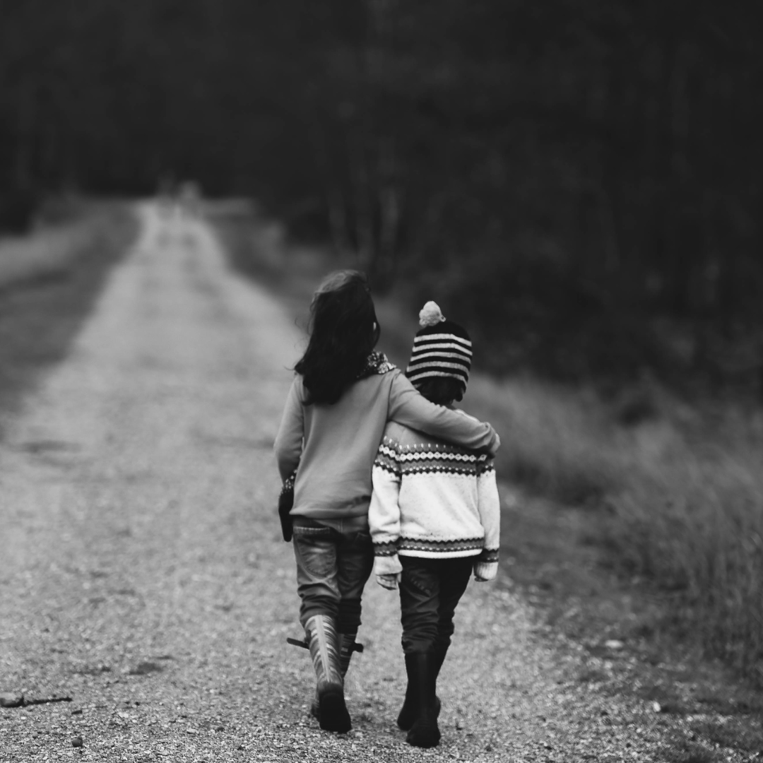 imagen a blanco y negro de una niña y un niño caminan abrazados por un camino rodeado de naturaleza. la imagen busca reflejar la importancia de las redes de apoyo desde la infancia