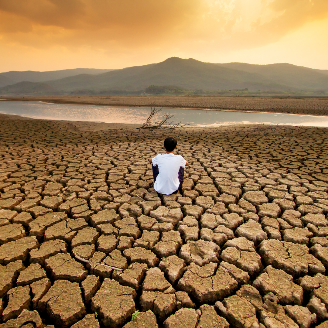 sobre un cuerpo de agua que esta totalmente seco hay una persona sentada mirando hacia lo poco que queda de agua. una imagen que refleja la relación entre la Salud Mental y el Cambio Climático