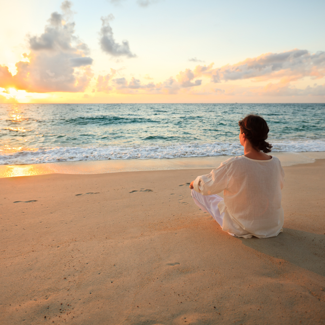 una mujer sentada en la orilla de la playa, viendo el amanecer. ejemplo del efecto Terapéutico del Mar